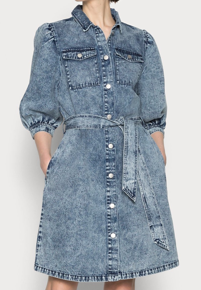 Denim-mekko nappilistalla, puffihäillä, rintataskuilla ja yhteensopivalla vyöllä, joka on solmittu vyötärölle.