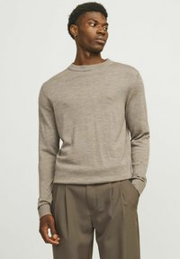Maglione beige chiaro in morbido tessuto a maglia, colletto rotondo, maniche lunghe e vestibilità slim. Abbinato a pantaloni beige con pieghe e tasche.