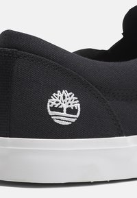Baskets en toile noires avec un logo d'arbre brodé blanc sur le côté, semelle en caoutchouc blanche et tissu texturé pour plus de durabilité.