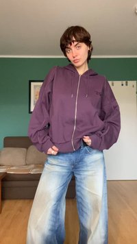 Paarse zip-up hoodie met oversized mouwen, voorzakken en een capuchon met trekkoord, gecombineerd met lichtgekleurde, versleten jeans met een wijde pijp.