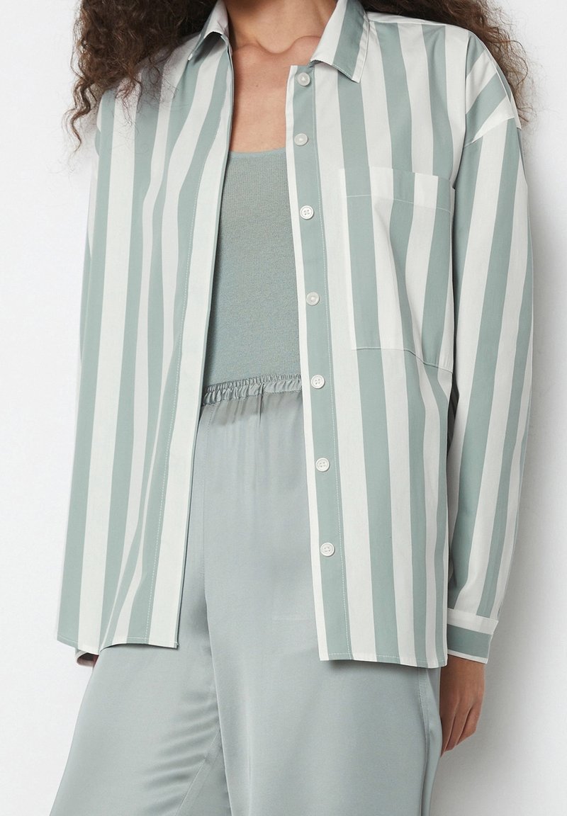 Camisa de botones a rayas verde claro y blanca con un bolsillo en el pecho, combinada con una blusa verde clara y pantalones de pijama a juego.