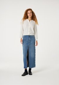 Witte geribbelde gebreide cardigan met knopen, gecombineerd met een lange denimrok met een zijsplit en knoopaccenten. Zwarte loafers gedragen.