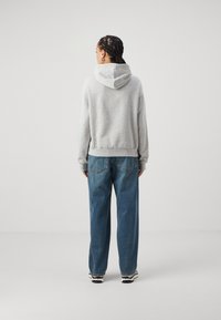 Gray hooded sweatshirt with a relaxed fit, worn with blue wide-leg jeans. Notable details include a drawstring hood and ribbed cuffs.