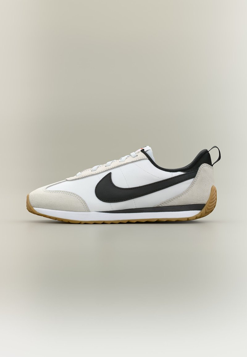 Άσπρο και μπεζ αθλητικό παπούτσι Nike με μαύρο λογότυπο swoosh, σόλα από καουτσούκ και μαύρο ταμπελάκι στη φτέρνα, εμφανίζεται από το πλάι σε ουδέτερο φόντο.