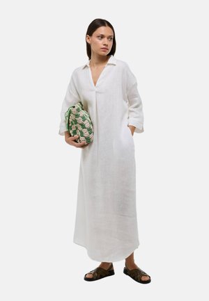 Robe en lin blanc avec un col et des manches trois-quarts, accompagnée d'un sac tissé vert et beige, et de sandales marron.
