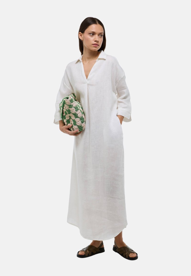 Robe en lin blanc avec un col et des manches trois-quarts, accompagnée d'un sac tissé vert et beige, et de sandales marron.