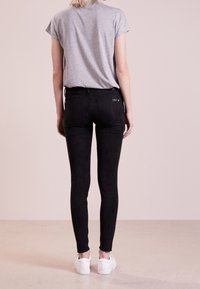 Jean skinny noir avec une texture douce, dotés de poches arrière et d'une coupe ajustée, associés à un t-shirt gris à manches courtes et des baskets blanches.