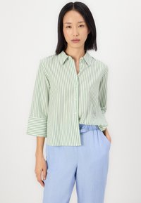 Gestreiftes Button-Up-Hemd in Grün und Weiß mit Dreiviertelärmeln und lockerer Passform. Hellblaue Hose mit elastischem Bund.