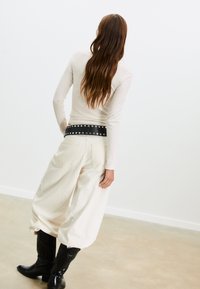 Maglietta a maniche lunghe crema abbinata a pantaloni oversized crema. Cintura di pelle nera con borchie visibile in vita. Stivali da cowboy neri completano il look.