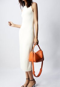 Valkoinen ribattudressi, jossa on hihaton malli, sivurei'ät, yhdistettynä rakenteelliseen oranssiin nahkalaukkuun ja mustiin nilkkahihnakenkiin.