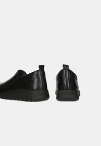 Scarpe slip-on in pelle nera con lati texturizzati, punta arrotondata e suola in gomma. Presentano una piccola linguetta sul tallone per facilitarne l'indosso.