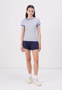 Ριγέ κοντομάνικο μπλουζάκι σε ανοιχτό μπλε και λευκό, με μπλε γιακά. Φορεμένο με σκούρες ναυτικές βερμούδες και λευκά αθλητικά παπούτσια. Απαλή υφή.