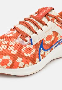 Biało-czerwony but do biegania w kwiaty z siateczkową cholewką, niebieskimi akcentami i amortyzowaną podeszwą. Posiada misternie zdobione sznurowadła.