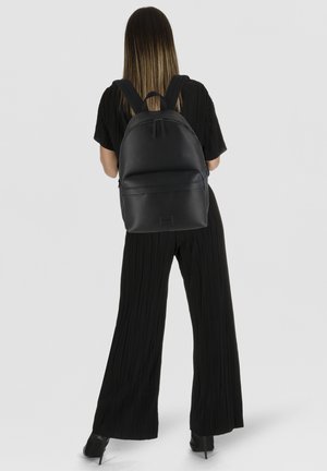 Zaino in pelle nera con forma arrotondata, superficie strutturata, due spallacci regolabili e una tasca frontale con cerniera.