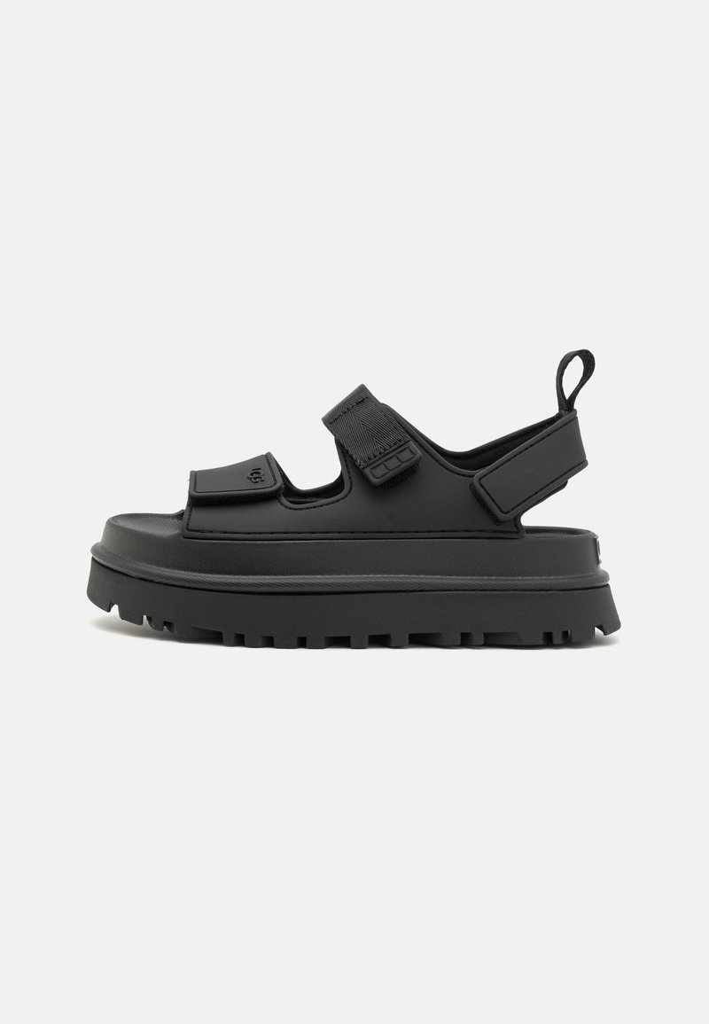Svart sandaler med tykk såle, justerbare stropper og teksturert overflate. Har en bakre stropp og en trekksløyfe for enkel påkledning.