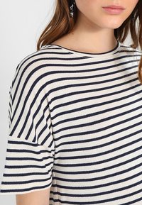 Koszulka w paski z kremowym tłem i granatowymi poziomymi paskami, krótkie rękawy oraz okrągły dekolt, wykonana z miękkiego materiału.