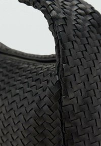 Sac en cuir tissé noir avec une finition texturée, doté d'une poignée incurvée et d'une fermeture à glissière sur le dessus, mettant en valeur un motif entrelacé détaillé.