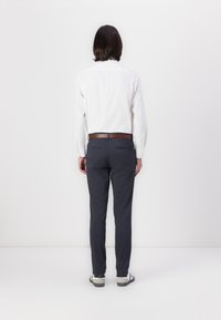 Chemise beige à boutons pour homme, pantalon navy, ceinture marron. Le pantalon possède des poches, la chemise a des manches longues et une coupe droite, tissu lisse.