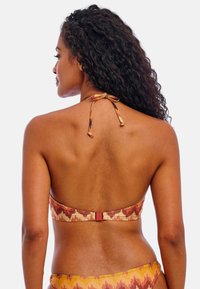 Bikini-top in gemusterde stof met warme kleuren van rood, oranje en geel; halternek met strik en haaksluiting op de rug.