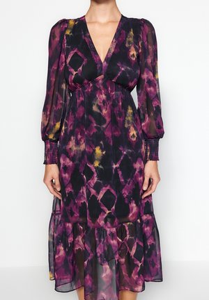 Lila-schwarzes Batik-Midikleid mit langen, transparenten Puffärmeln, V-Ausschnitt, gerafften Bündchen und Rüschensaum, getragen von einer stehenden Person