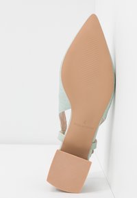 Semelle d'une chaussure vert clair à bout pointu avec un talon carré beige, taille 4, avec "Made in China" imprimé sur la semelle.