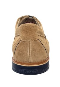 Beige suède schoen met een ronde hak, voorzien van marineblauwe stiksel en een gestructureerde rubberen zool. Mernaam "Fluchos" zichtbaar op de zool.