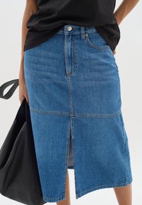 Jeanskjol i ljusblått med en framfickslits, midilängd, femficksdesign och kontrasterande sömmar. Bärs med en svart topp och väska.