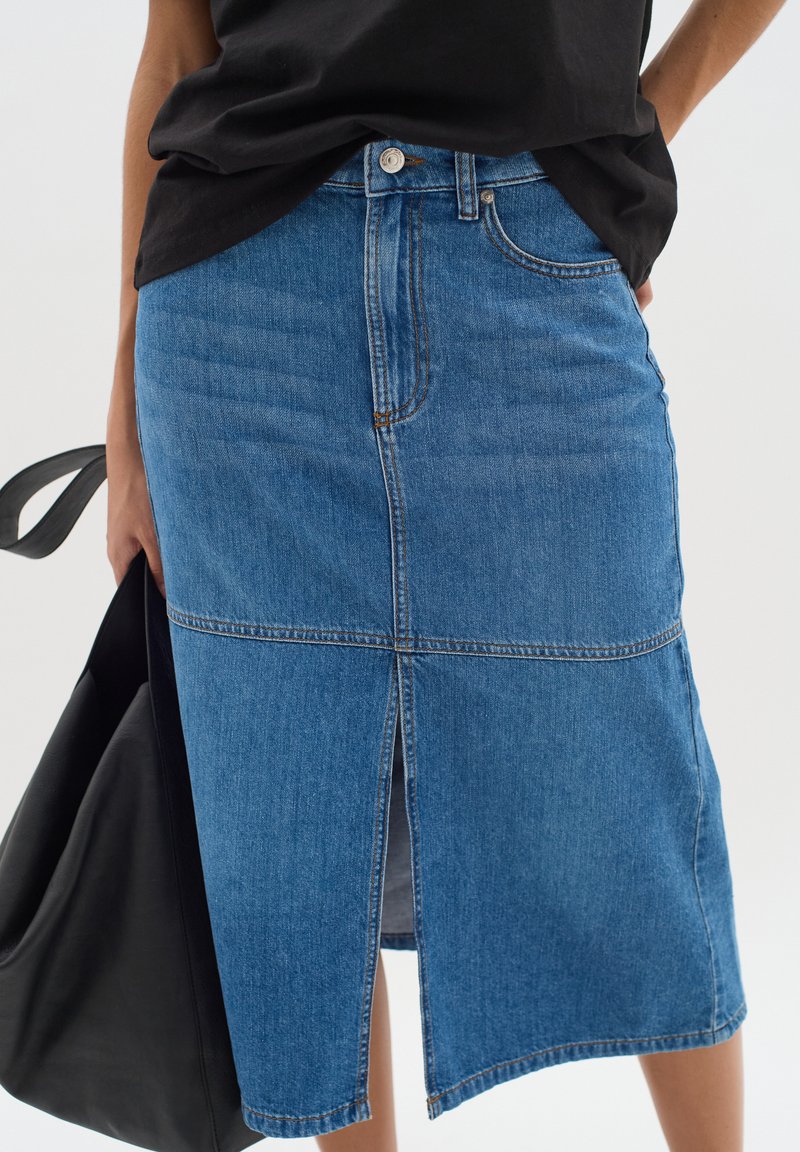 Jeanskjol i ljusblått med en framfickslits, midilängd, femficksdesign och kontrasterande sömmar. Bärs med en svart topp och väska.