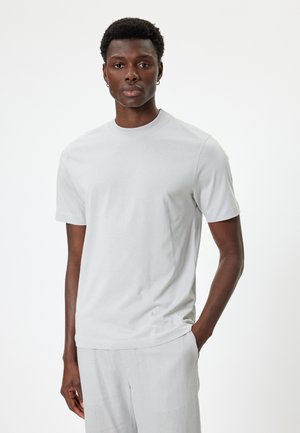 Lichtgrijze t-shirt met korte mouwen, gemaakt van een gladde stof, met een ronde halslijn en een relaxte pasvorm. Gecombineerd met lichtgrijze broek.