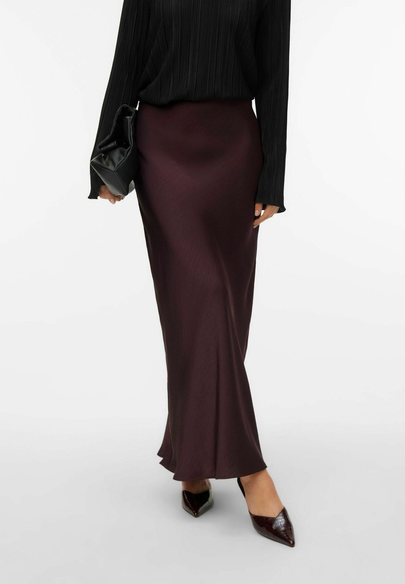 Lang burgunderrød satin nederdel med en flydende silhuet, parret med en sort tekstureret bluse. Accessoriseret med en sort clutch og glossy spidse sko.