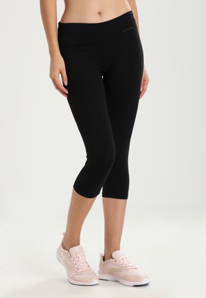 Schwarze Capri-Leggings mit einem breiten Bund und glatter Textur, kombiniert mit hellrosa Sportschuhen mit Schnürdesign und kontrastierenden Akzenten.