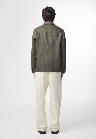 Olijfgroene, langemouwen shirt met een gladde textuur en een kraag, gecombineerd met lichtbeige, loszittende, verticaal gestreepte broeken.