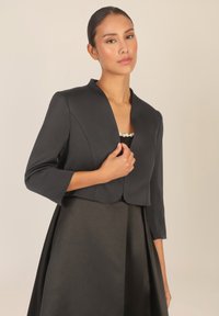 Mustat lyhyet takit, joissa on kolme neljäsosaa hihat, joissa on shaalikaulus ja sileä pinta, yhdistettynä tyylikkääseen, samasta kankaasta valmistettuun hameeseen.