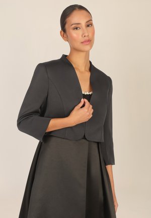 Schwarze kurz geschnittene Jacke mit Dreiviertelärmeln, ausgestattet mit einem Schalkragen und glatter Textur, kombiniert mit einem eleganten, passenden Rock.