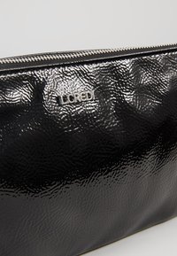 Pochette texturée noire avec fermeture éclair argentée et logo "LCREDI" argenté sur le devant, présentée sur un fond uni.