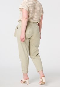 Jeans tapered taille haute, vert clair, avec des ourlets roulés et des poches arrière, associés à un haut en tricot beige et des sandales à talons carrés nude.