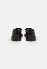 Black leather loafers with a smooth texture, low heel, and minimal stitching detail, viewed from the back.