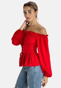 Top rosso a spalle scoperte con maniche a sbuffo, vita svasata e orlo arricciato; realizzato in tessuto morbido con dettagli in pizzo decorativi.