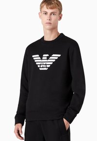 Felpa nera con polsini e orlo a coste, caratterizzata da un grande logo bianco a righe sul davanti. Design classico con colletto rotondo, texture liscia.