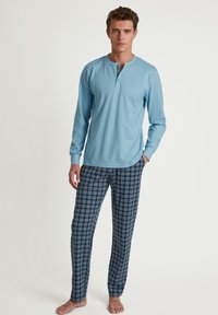 Lichtblauw langslievend shirt met een henley halslijn, gecombineerd met donkerblauwe geruite pyjamabroek met verticale en horizontale lijnen.