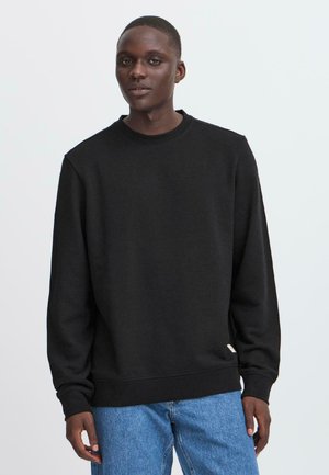Zwarte sweatshirt met een ronde hals en lange mouwen, met een relaxte pasvorm en ribbelmanchetten. G gecombineerd met lichtblauwe denim jeans.