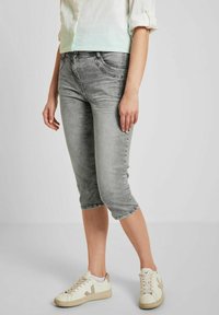 Pantalones capri de mezclilla gris con una textura desgastada, ajuste de cintura media y dobladillos enrollados, combinados con zapatillas blancas para un look casual.
