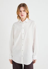White long-sleeve shirt made of lightweight fabric, featuring a button-down front, classic collar, and slightly oversized fit with cuffed sleeves.