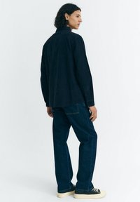 Marineblauw overhemd met knopen, een kraag, lange mouwen en een losse pasvorm. Gecombineerd met donkere denim jeans en sneakers met crèmekleurige zolen.