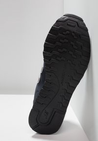 Suela de goma negra de una zapatilla con un patrón de relieve texturizado, que presenta un upper azul oscuro con un acento de logo plateado.