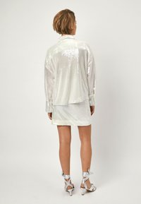 Iridescent, pailletten shirt en mini-rok set, met een losse pasvorm en lange mouwen, gedragen met zilveren sleehakken.