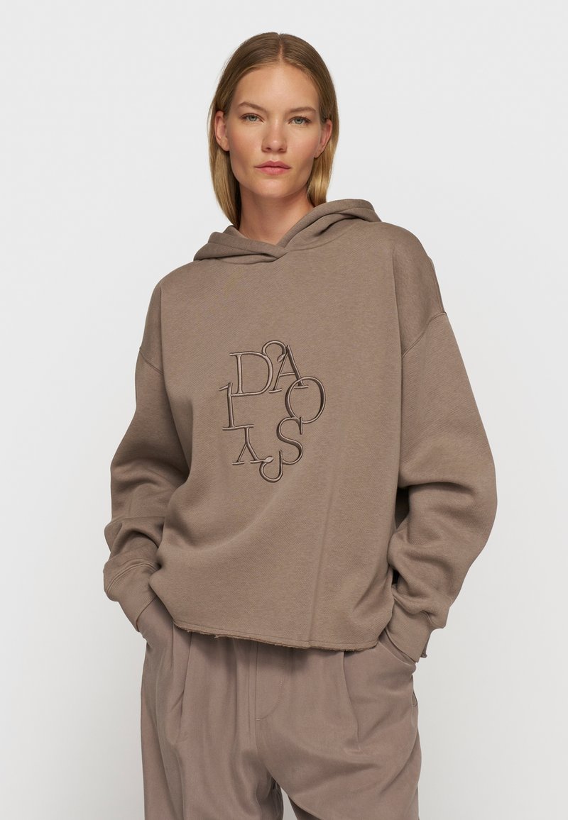 Bruine, cropped hoodie met een trekkoordcapuchon en een oversized pasvorm. Bevat een gestikte geometrische logo in een donkere tint. Zachte stoftextuur.