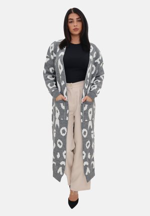 Langer grauer Strickcardigan mit weißen Leopardenflecken, ausgestattet mit einem Schalkragen, seitlichen Taschen und gerippten Bündchen. Getragen über einem schwarzen Oberteil.