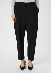 Pantaloni negri, croiți la comandă, cu talie înaltă, pliuri, buzunare laterale și un design cu picioare tapered. Purtați cu pantofi cu toc ascuțit, negri.