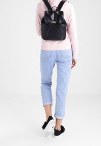Svart quiltad läderryggsäck med dragsko, platt toppflik och justerbara remmar. Avslappnade ljusblå jeans med uppvikt fåll och svarta skor.